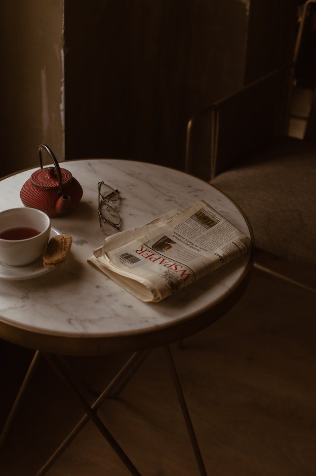 comfortable chair near round table with newspaper and tea set