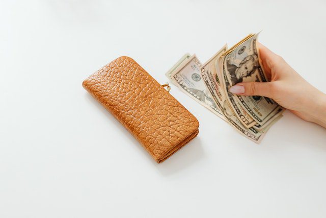 Pexels - Person holding money on white table beside a wallet