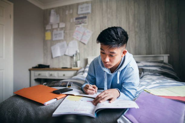 Teenage boy lying on his bed while concentrating on homework for his exams.