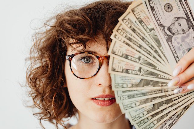 Pexels - Woman in eyeglass covering her face with paper money