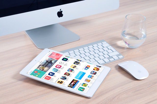 mac monitor with keyboard and mouse and glass of water and tablet.