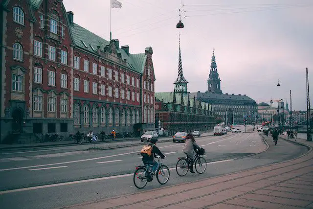 Cyclists riding along wide embankment near historic buildings in city