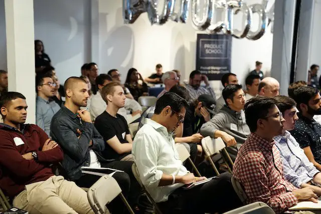 People sitting in an audience listening to a presentation at a conference