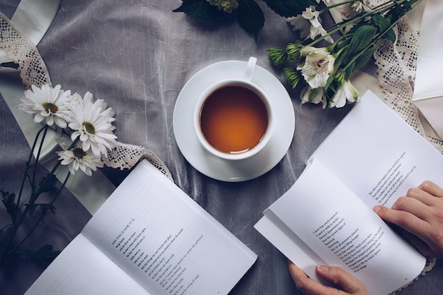 Woman reading a book with tea and flowers.