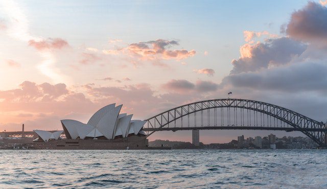 Stylish modern building and arch bridge crossing harbor against cloudy sundown sky