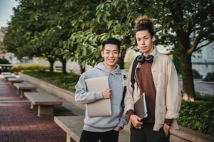 Multiethnic male students standing with laptop and folder in park