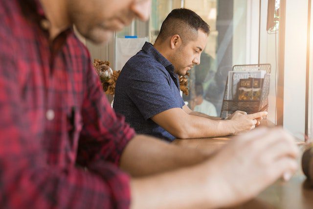 Man Using Smartphone Sitting Beside Table and Man