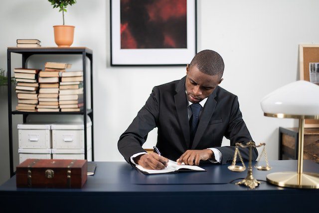 A Man in a Suit Writing on a Notebook in His Office