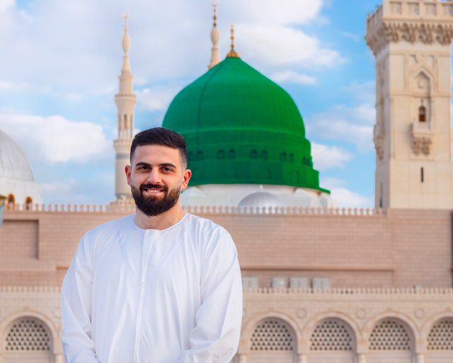 man in white long sleeve shirt standing near a mosque