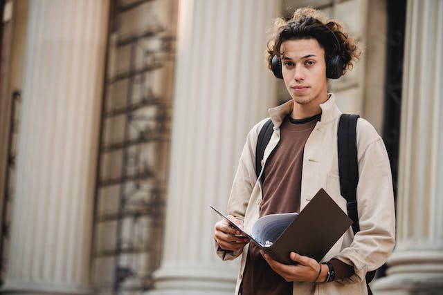 serious student in wireless headphones with folder