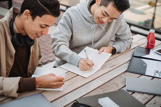 crop positive diverse male students working on assignment in park