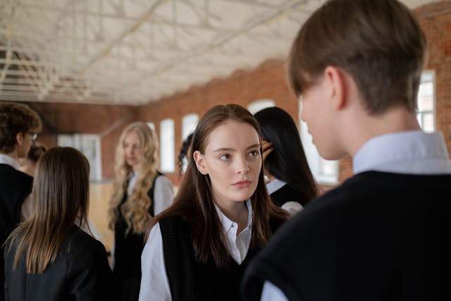 young woman in black sweater vest staring at a young man
