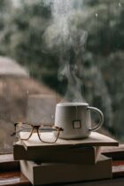 cup of tea and an eyeglasses on the stacks of books near the window