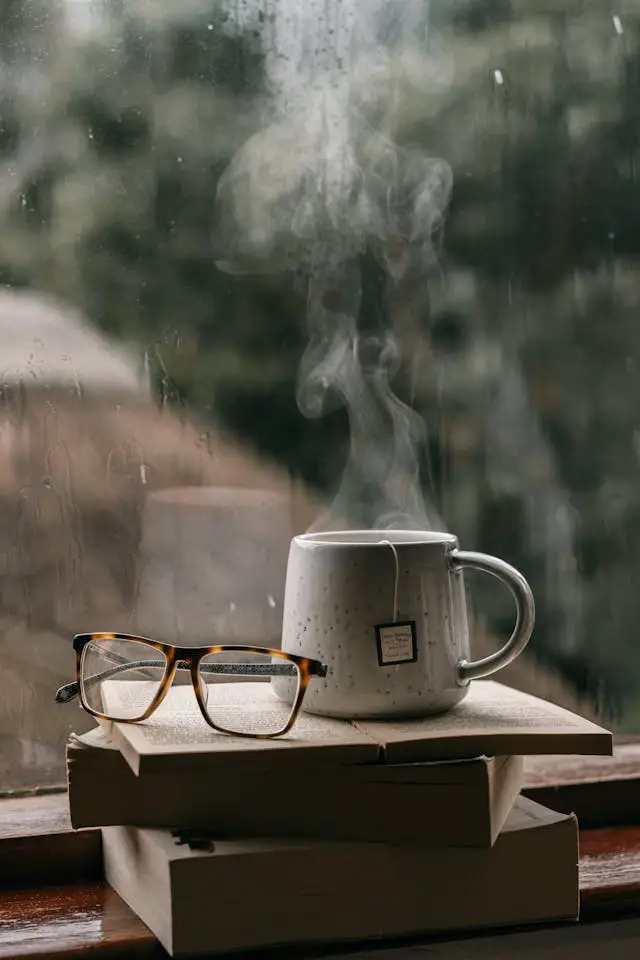 cup of tea and an eyeglasses on the stacks of books near the window