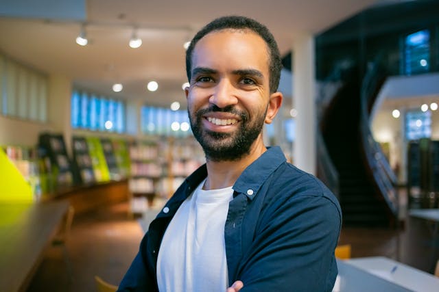 positive ethnic male student standing in modern library