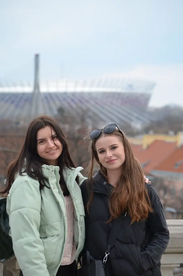 two women standing next to each other in front of a stadium