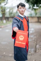 young graduate holding certificate outdoors