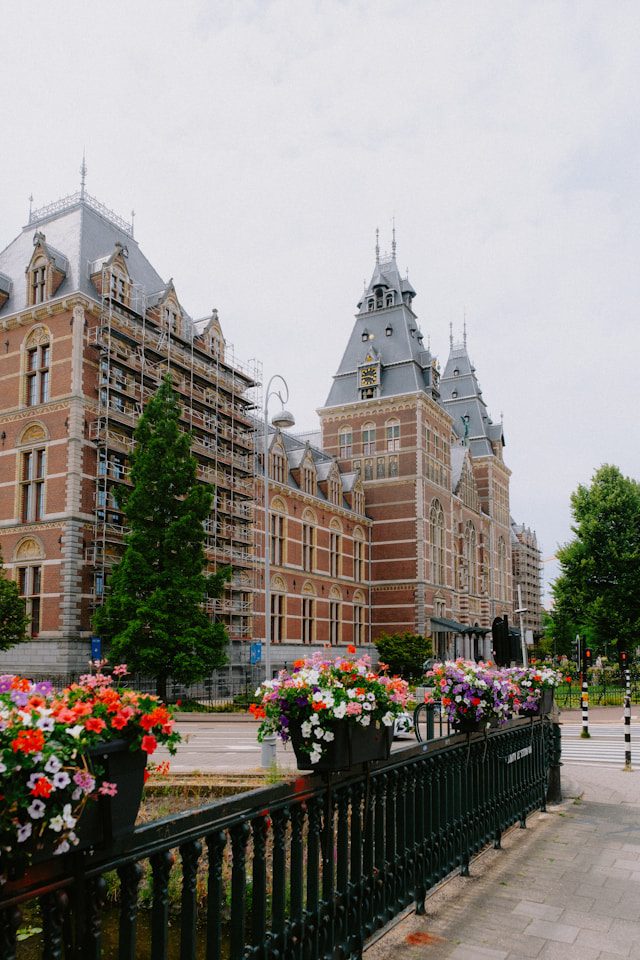 a large building with a fence and flowers in front of it